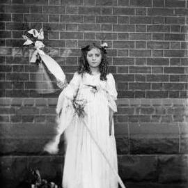A girl holding a wand and standing on a rug in front of a wall.  Family name Adams.