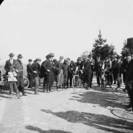 Two cyclists with supporters and onlookers.