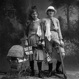 Studio portrait of two young women holding flags and dressed in costumes.   Family name Davies.