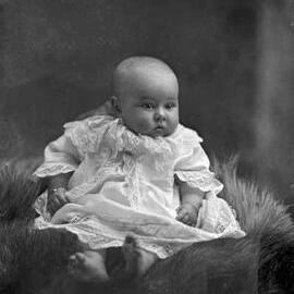 Studio portrait of a baby wearing a dress.  Family name possibly May.
