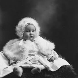 Studio portrait of a baby wearing a fur trimmed bonnet and cape.  Family name Rowell or Howell.