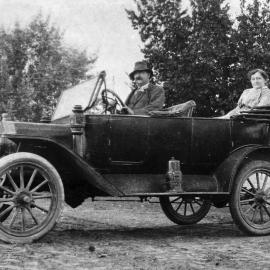 An open touring car with male driver and female passenger.