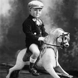 Studio portrait of a young boy seated on a rocking horse.  Family name Rogers.