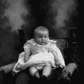 Studio portrait of a baby wearing a lace dress.   Family name McNamara.