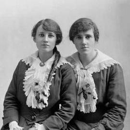 Portrait of two young seated women wearing flowers.