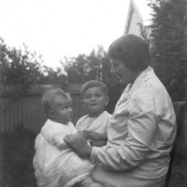 An informal outdoor portrait of a seated woman and two young children.