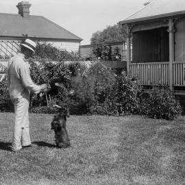 An unidentified man playing with a dog in front of a house named Warrawee.