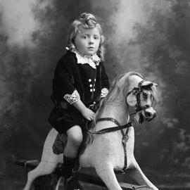 Studio portrait of a girl on a rocking horse.  Family name Fisher.