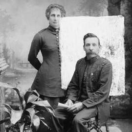 Studio portrait of a seated man and a standing woman.  Family name Leonard.