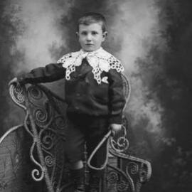 Studio portrait of a boy wearing a suit and lace collar.