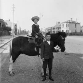 Two unidentified boys with a horse in an urban environment.