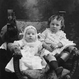 Studio portrait of a baby and a young child seated together.  Family name Price.