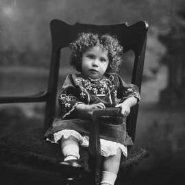 Studio portrait of a young girl in an embroidered dress.  Family name Bussell.