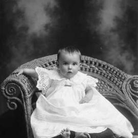 Studio portrait of a baby seated on a cushion. Family name Speedie.