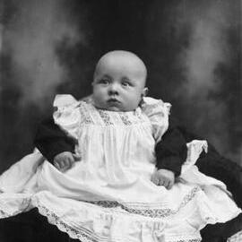 A studio portrait of a baby seated on a cushion.  Family name Rawlings.