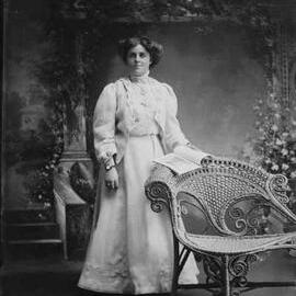 Studio portrait of a young woman standing at a wicker chair.