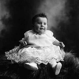 Studio portrait of a baby wearing a dress.  Family name Baker.