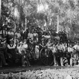 A posed group of about 50 male workers in a forest environment.