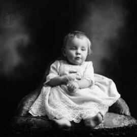 Studio portrait of a baby wearing a dress.  Family name Johns.