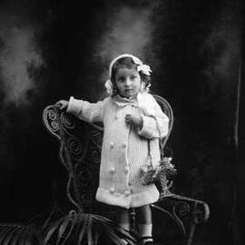 Studio portrait of a young girl in a knitted dress and bonnet. Family name Kendall.