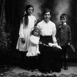 Studio portrait of a seated woman with three children.  Family name Earl.