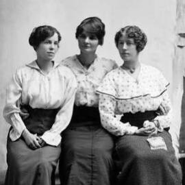 Studio portrait of three young women, each wearing a blouse and long skirt.