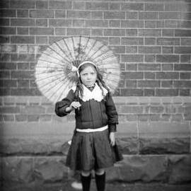 A young girl standing outdoors on a rug in front of a wall.  Family name Dougherty.