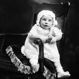 Studio portrait of a baby wearing a bonnet and dress.  Family name Gavan or Gaven.
