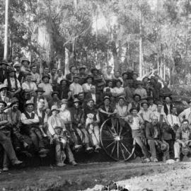 A posed group of about 50 male workers in a forest environment.