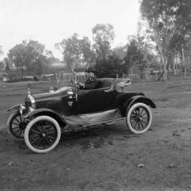 A man at the wheel of an open coupe car.