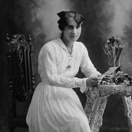 Studio portrait of a young woman seated on a high backed chair.  Family name Quick.
