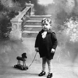 Studio portrait of a boy with a pull-along toy horse.  Family name ‘Goddard’.