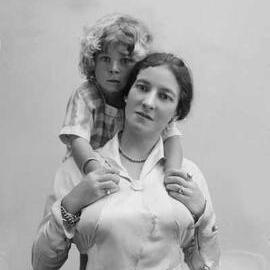 Studio portrait of a woman supporting a young child on her shoulders.  Family name Perry.