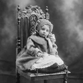 Studio portrait of a baby girl wearing a coat and hood.  Family name Winrow.