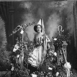 A young woman in costume standing amongst  flowers.  Family name Cullen or Cutler.