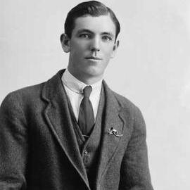 Studio portrait of a young man wearing a suit and a brooch on his lapel.