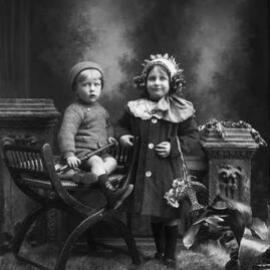 Studio portrait of a girl standing alongside a seated boy.  Family name Hardiman.