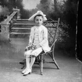 Studio portrait of a boy wearing a triangular hat and holding flowers.