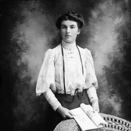 Studio portrait of a woman standing at a wicker chair.  Family name Roberts.