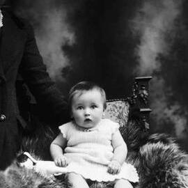 Studio portrait of a baby wearing a knitted dress.   Family name McCoy.
