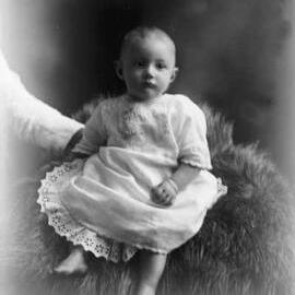 Studio portrait of a baby wearing a dress.  Family name Cleary.