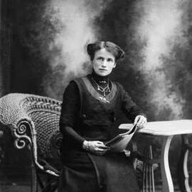 Studio portrait of a woman seated in a wicker chair.  Name Miss McInerny or similar.