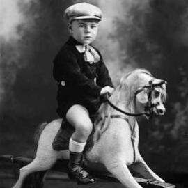 Studio portrait of a young boy seated on a rocking horse.  Family name Rogers.