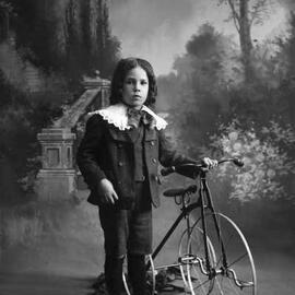 Studio portrait of a boy with a tricycle. Family name Robert or Rolent.