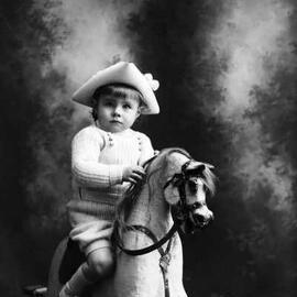A studio portrait of a young boy siting on a rocking horse.