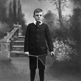 Studio portrait of a boy holding a stringed racquet.  Family name Merry.