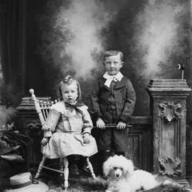 Studio portrait of a young boy and girl with a poodle dog.
