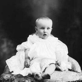 Studio portrait of a baby seated on a cushion.   Family name Fountain.