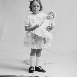 Studio portrait of a girl holding a large doll.   Family name Carmody.