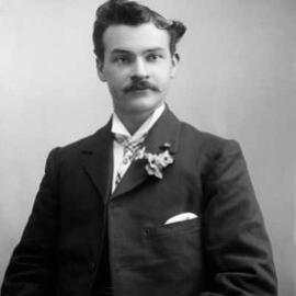 Portrait of a young man wearing a sprig of flowers in his button hole.